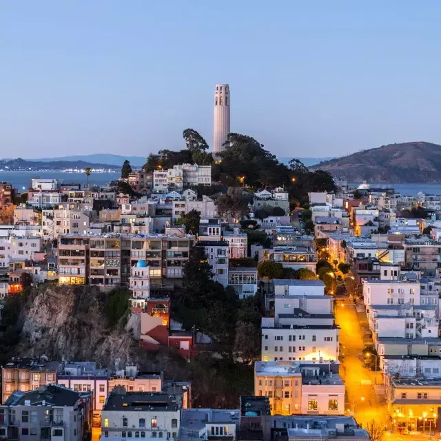 黄昏时分的贝博体彩app科伊特塔, with lighted streets before it 和 the San Francisco Bay behind it.